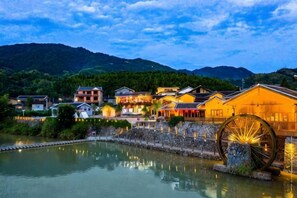 A traditional building with a large water wheel, surrounded by a body of water and greenery, with mountains in the background. - Waiting For You at Yunshuiyao Inn (Nanjing County)