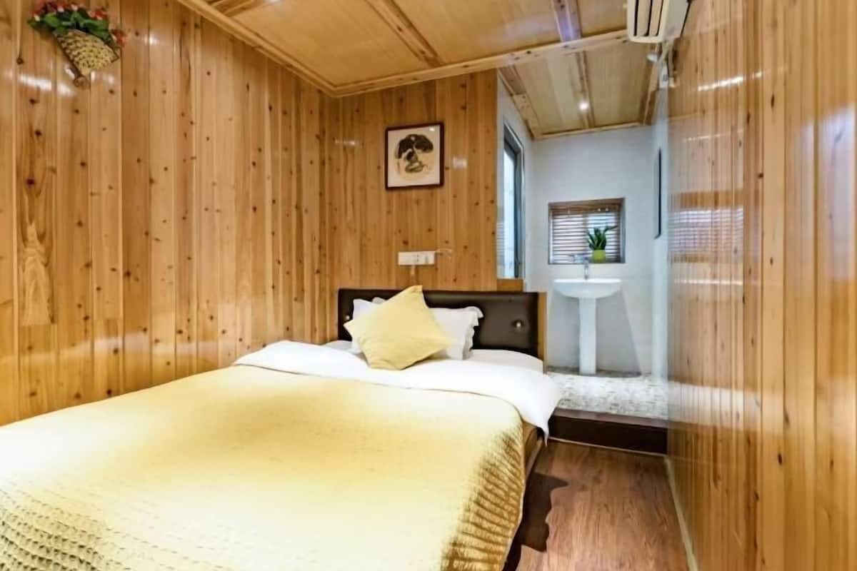 A wooden-paneled room with a bed, a bedside table, a small window, and a wall-mounted picture.