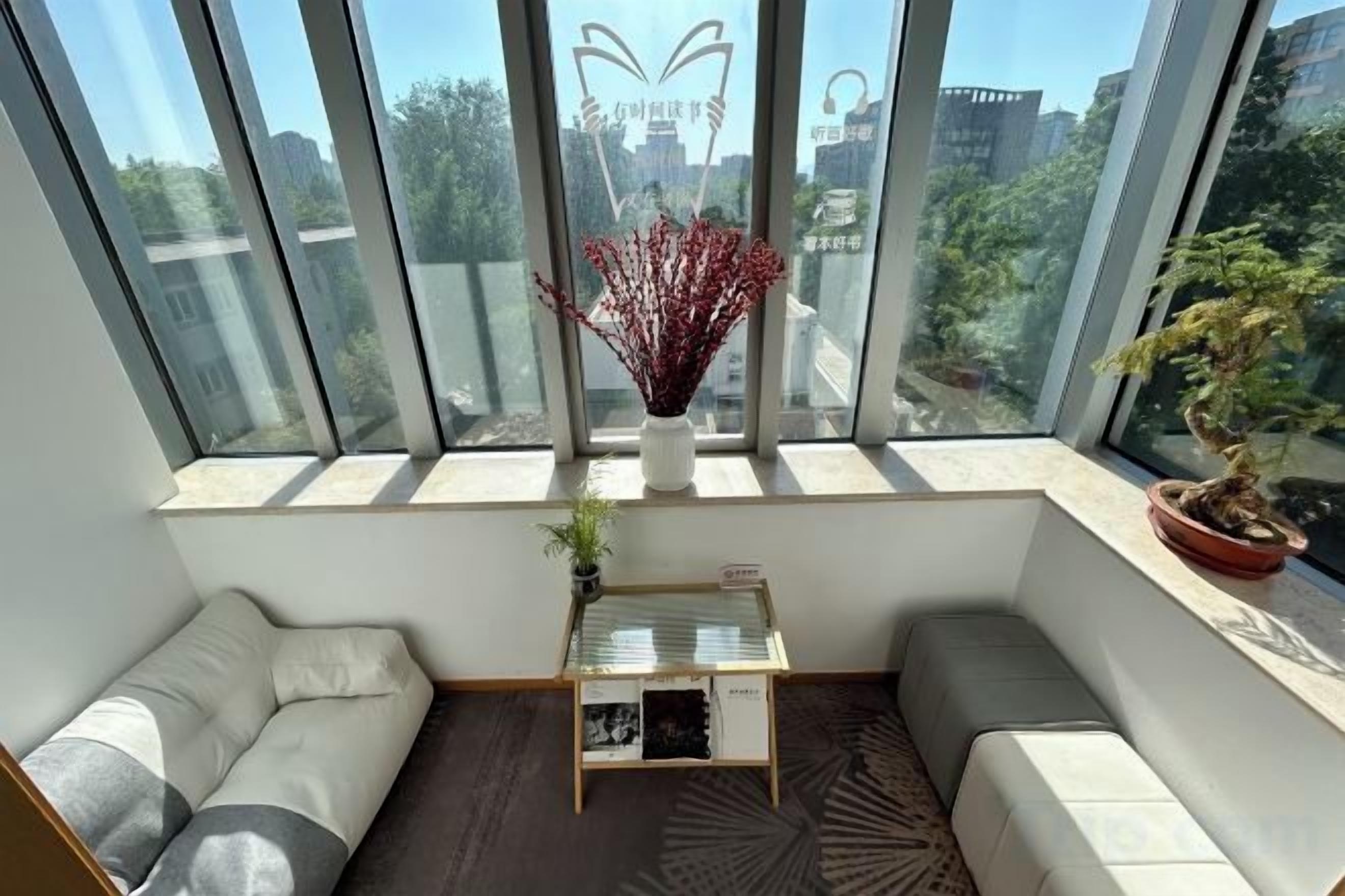 A modern room with a large window, a sofa, a small table, and a potted plant.