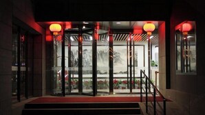 A hotel entrance with a red carpet, glass doors, and red lanterns.
