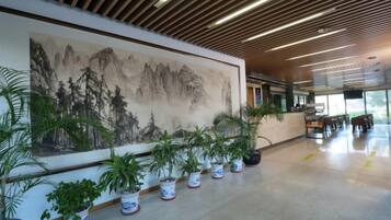 A spacious lobby with a large wall-mounted painting, potted plants, and a modern ceiling design.