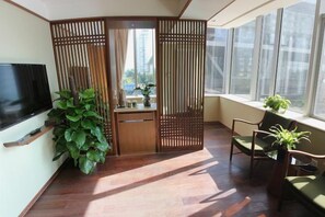 A room with a TV, wooden partition, chairs, and a large plant. - National Library Hotel (Beijing)