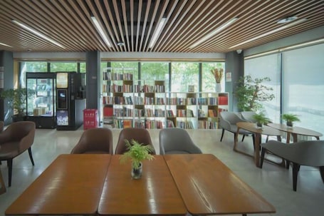 A modern library with a wooden ceiling, bookshelves, and seating areas.. National Library Hotel