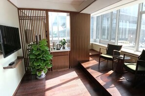 A modern room with a TV, a potted plant, a small table, and chairs near a large window. - National Library Hotel (Beijing)