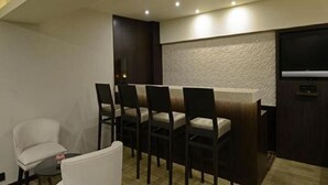A modern dining area with a bar, dark wooden chairs, a white cushioned chair, and a flat-screen TV mounted on the wall.
