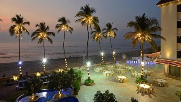 A resort with a pool, outdoor seating, palm trees, and a view of the beach at dusk.