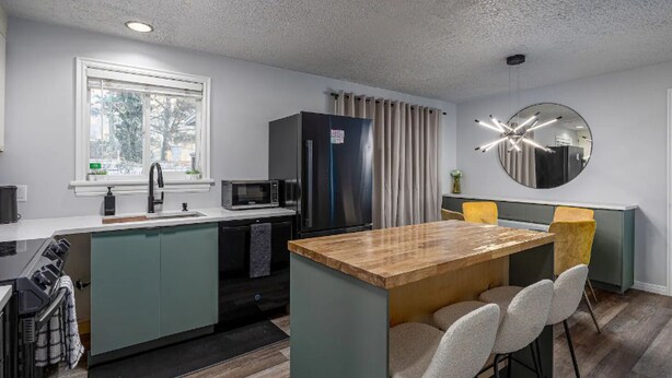 A modern kitchen with a central island, a microwave, a refrigerator, and a dining area with chairs and a table. - NEW! Charming Duplex - Central, Ski, Hike, Unwind! (Sandy)