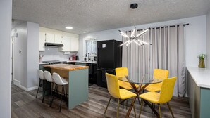 A modern kitchen with a central island, bar stools, and a dining area with yellow chairs. - NEW! Charming Duplex - Central, Ski, Hike, Unwind! (Sandy)