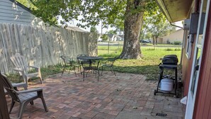 Een terras met bakstenen vloer, een tafel, stoelen, een barbecue en een boom.