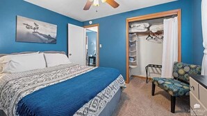 Een slaapkamer met een bed, een stoel, een kledingkast en een plafondventilator.