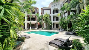 Une cour avec une piscine, des chaises longues et une végétation luxuriante.