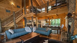 Ein geräumiges Blockhäuschen mit einer Holztreppe, einem blauen Sofa, einem Esstisch und einem Kamin aus Naturstein.