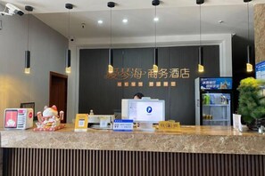 A hotel reception desk with a computer, a cash register, and a small plant.