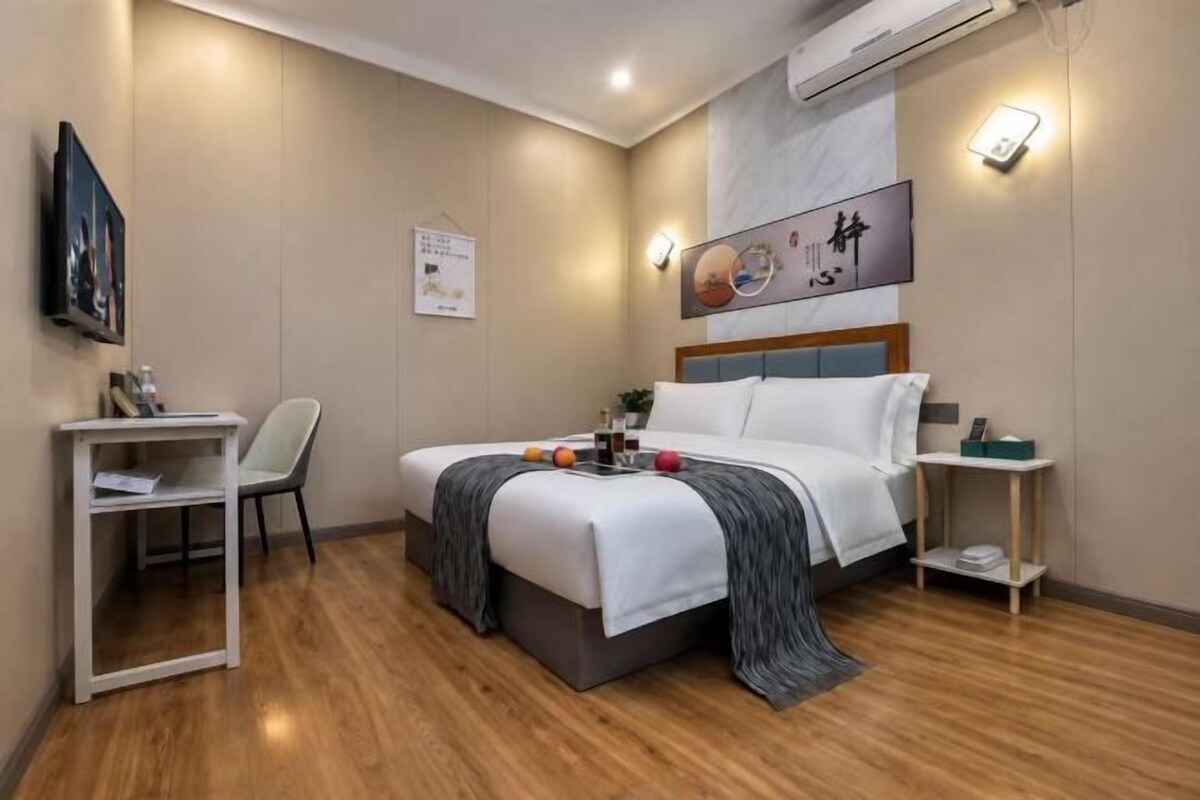 A hotel room with a bed, bedside table, chair, and a desk with a chair.