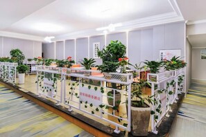 A hotel reception area with a long reception desk, potted plants, and a white railing.