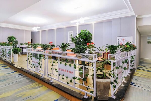 A hotel reception area with a long reception desk, potted plants, and a white railing.