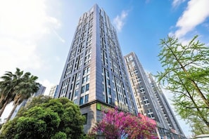 A high-rise building with multiple floors, surrounded by greenery and other tall structures. - Aegean Business Hotel (Chongqing Auto Expo Center Branch) (Chongqing)