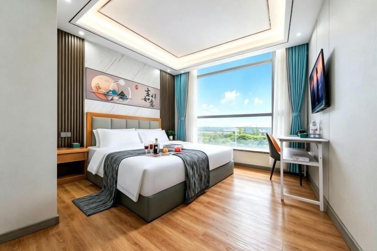 A modern hotel room with a large bed, a desk, and a view of the outdoors.