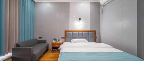 A hotel room with a bed, a nightstand, a sofa, and an air conditioning unit.