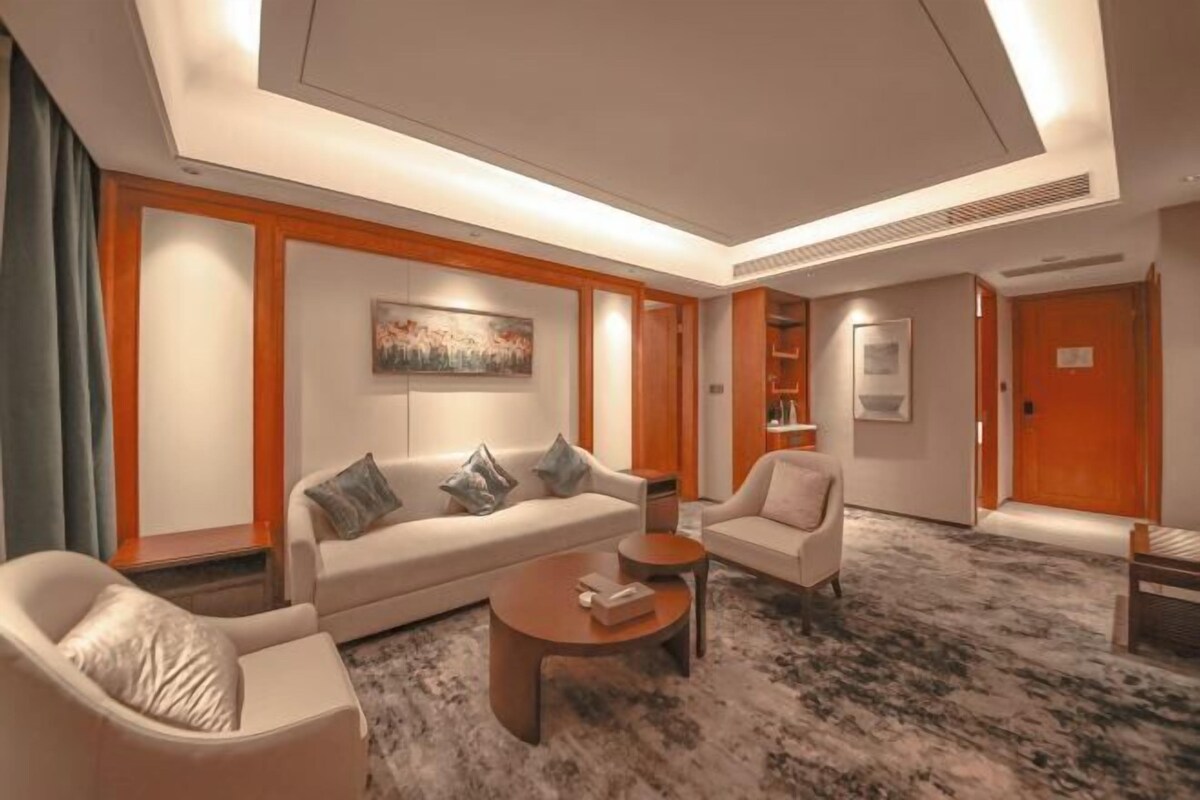 A modern hotel room with a sofa, armchairs, a coffee table, and a carpeted floor.