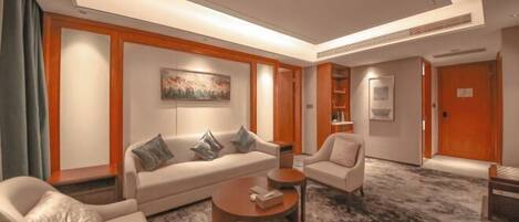 A modern hotel room with a sofa, armchairs, a coffee table, and a carpeted floor.