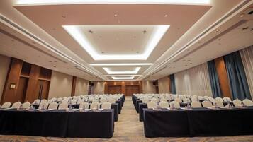 A conference room with rows of tables and chairs, a carpeted floor, and a modern ceiling design.