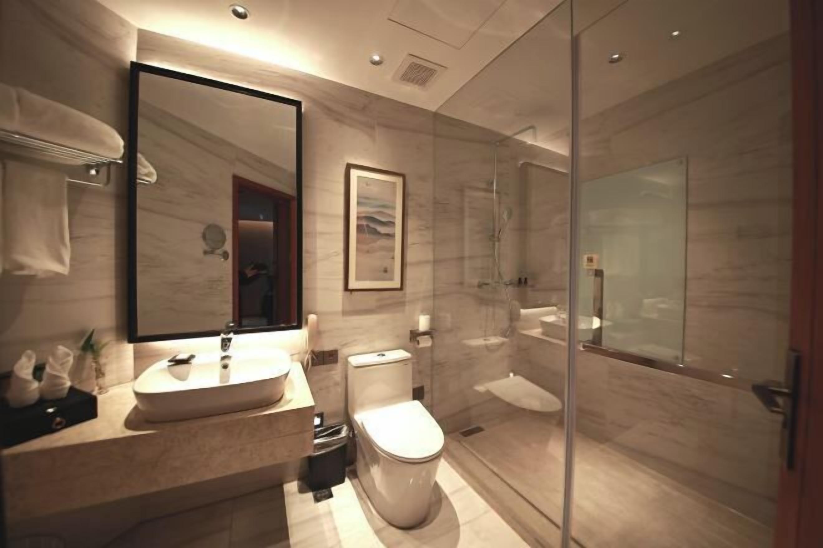 Un baño moderno con un espejo grande, un lavamanos, un inodoro y una zona de ducha con mampara de vidrio.