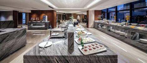 Un moderno vestíbulo de hotel con un mostrador de recepción de mármol, una larga barra de buffet y un área de descanso.