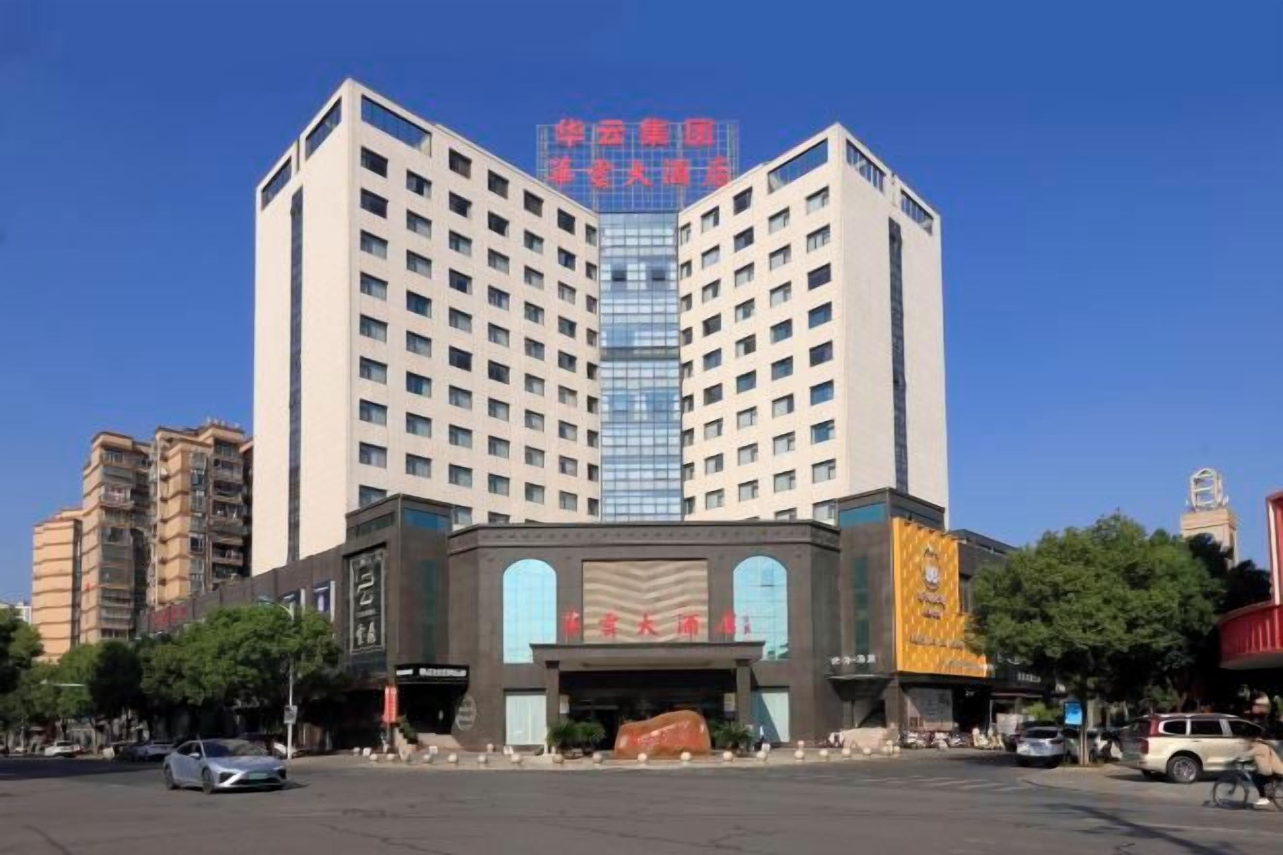 A multi-story hotel with a central entrance, surrounded by other buildings, and a clear sky.