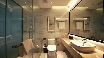 Un baño moderno con cabina de ducha de vidrio, inodoro, lavamanos y un espejo grande.