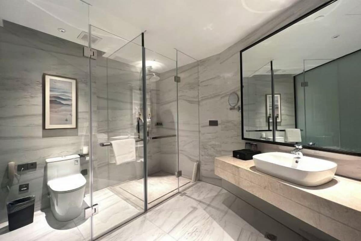 A modern bathroom with a glass-enclosed shower, a toilet, a sink, and a large mirror.