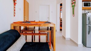 A compact living space with a wooden dining table, benches, a sofa, and a kitchen area with a refrigerator and microwave. - Beautiful ocean-view 2 bedroom home in Fumba Town (Fumba Town)