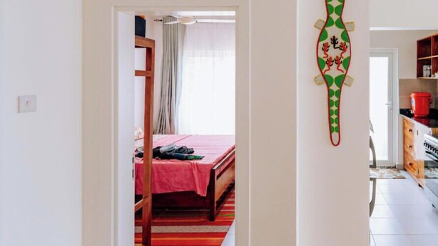 A room with a bed, a wooden wardrobe, and a kitchen area visible through an open door. - Beautiful ocean-view 2 bedroom home in Fumba Town (Fumba Town)