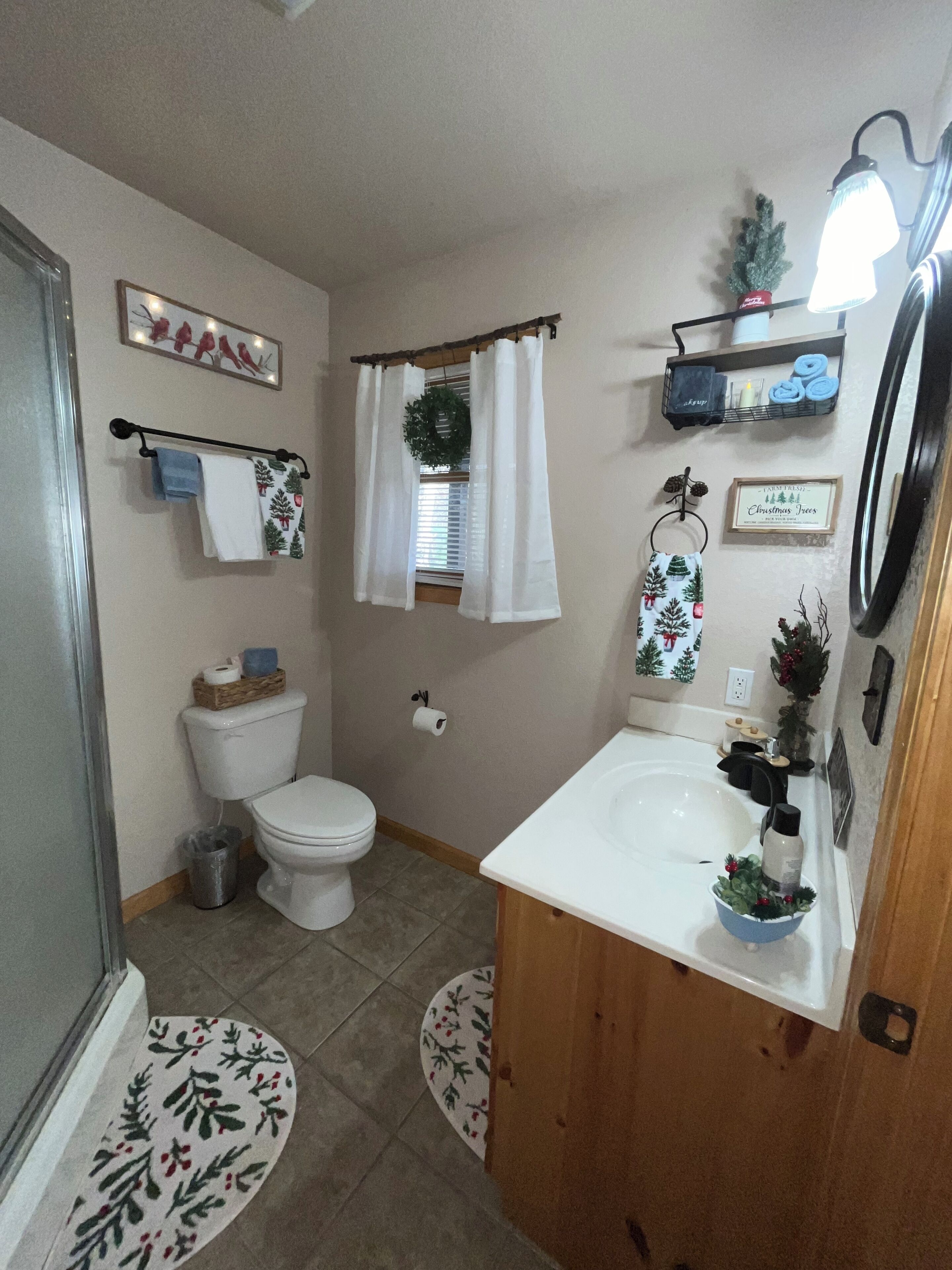 Een badkamer met toilet, wastafel en douche. Handdoeken hangen aan een rek, er is een douchegordijn en een kleine kerstversiering.