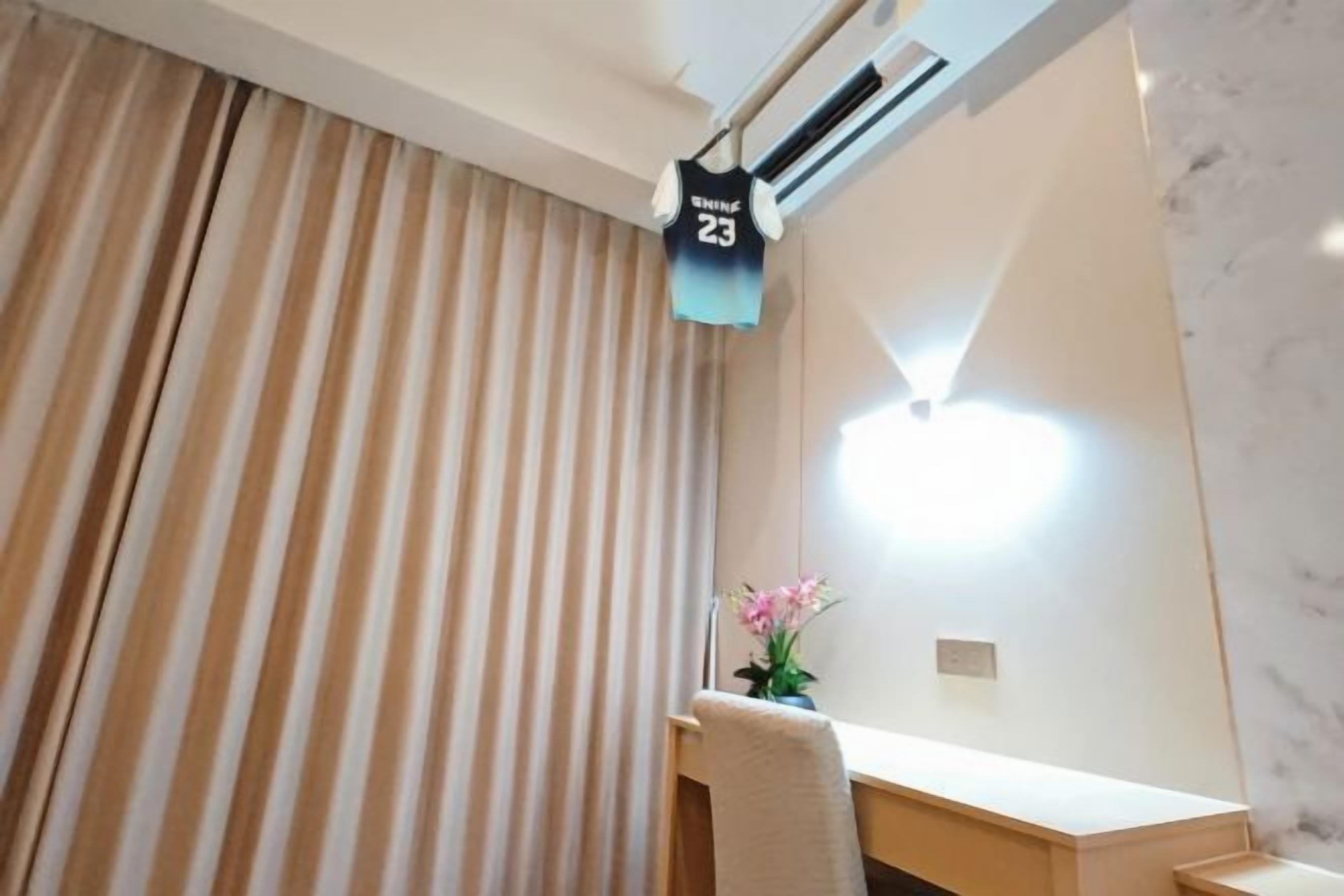 Habitación de hotel con cama, mesita de noche con lámpara, ventana con cortinas y aire acondicionado de pared.