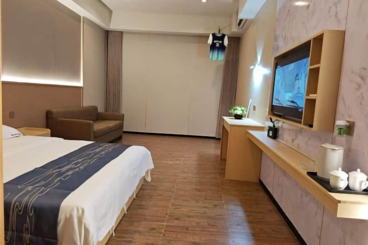 Habitación de hotel con cama, escritorio, televisor y zona de estar.