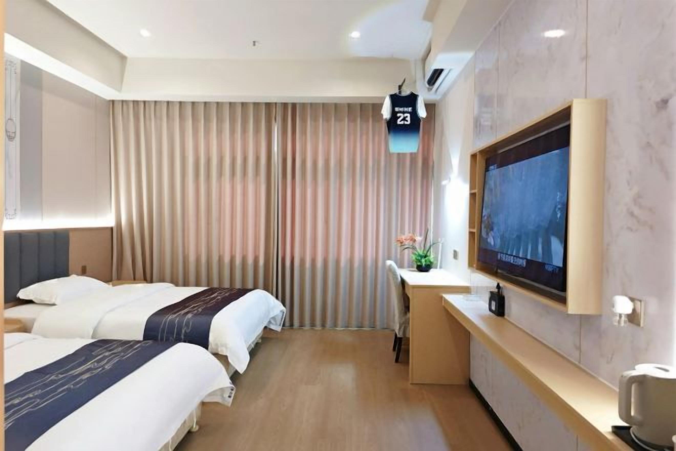 A hotel room with two beds, a desk, a TV, and a curtain.