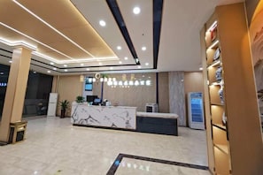 Zona de recepción de un hotel, con mostrador de mármol, una pantalla digital y un expendedor.