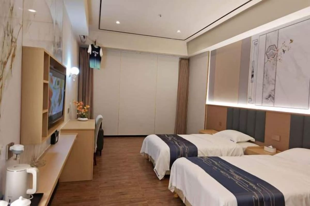 Habitación de hotel con dos camas, un escritorio, un televisor y un ventanal amplio.