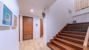 A staircase with wooden steps leading to a landing, a wooden door, and a wall-mounted light fixture. - Chiang Mai Colonial House (Tambon San Phi Suea)