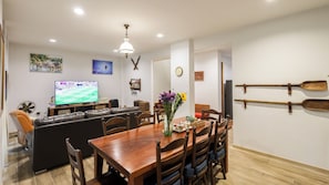 A dining area with a wooden table, chairs, a television, and a clock on the wall.