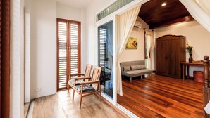 A room with a wooden floor, a sofa, a chair, a table with a vase, and a wardrobe. - Chiang Mai Colonial House (Tambon San Phi Suea)
