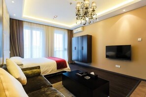 A modern hotel room with a bed, sofa, TV, and a chandelier.