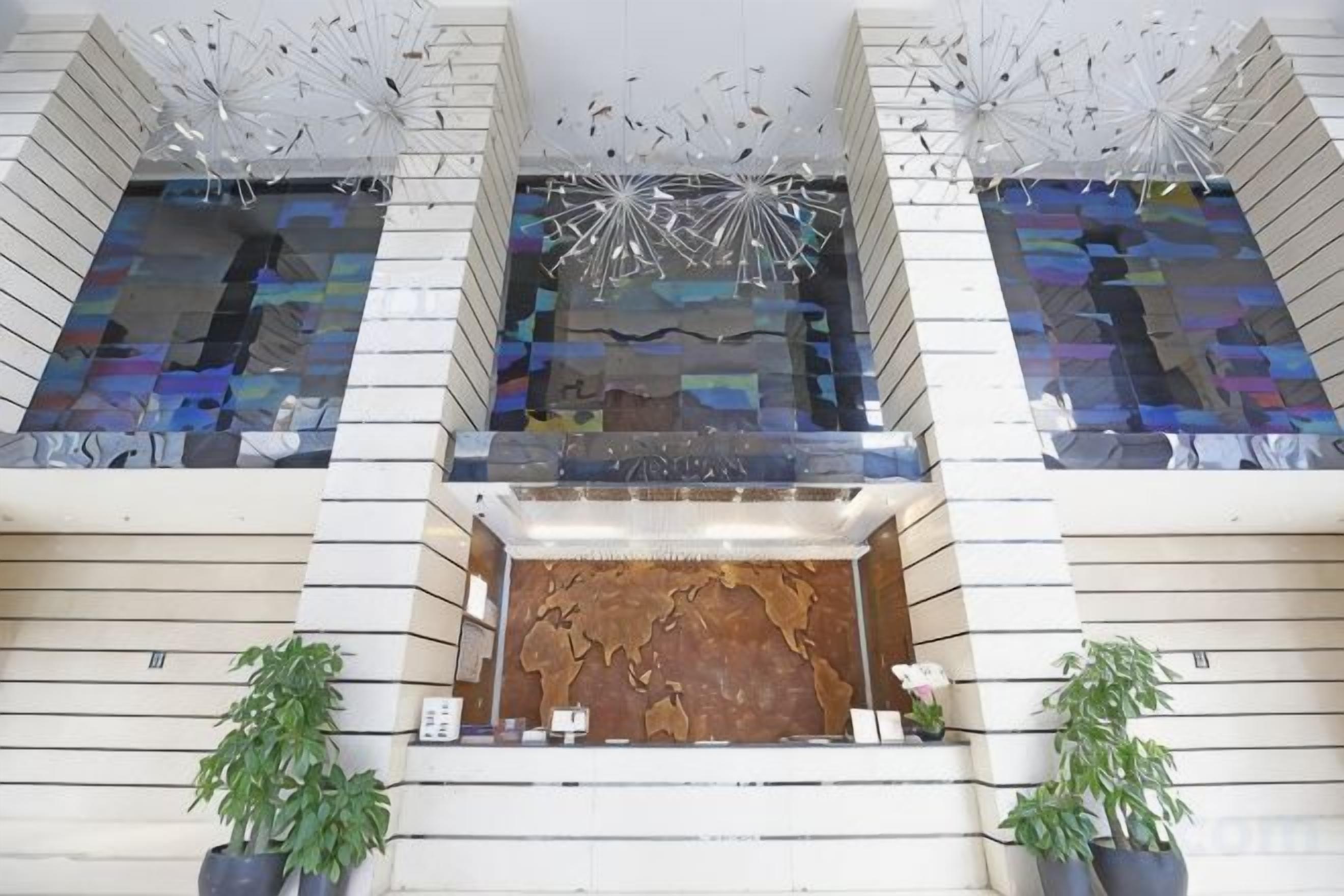A lobby with a central staircase, two potted plants, and a decorative ceiling feature.