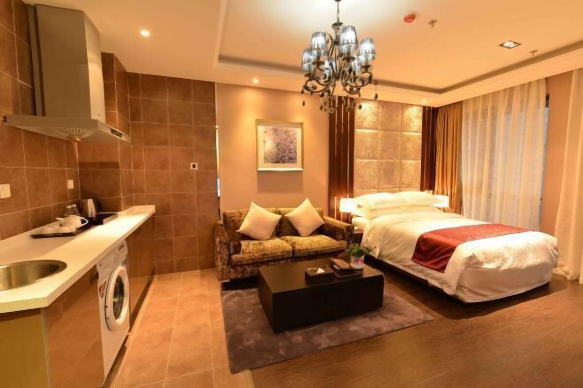 A hotel room with a bed, a sofa, a coffee table, a washing machine, and a chandelier.