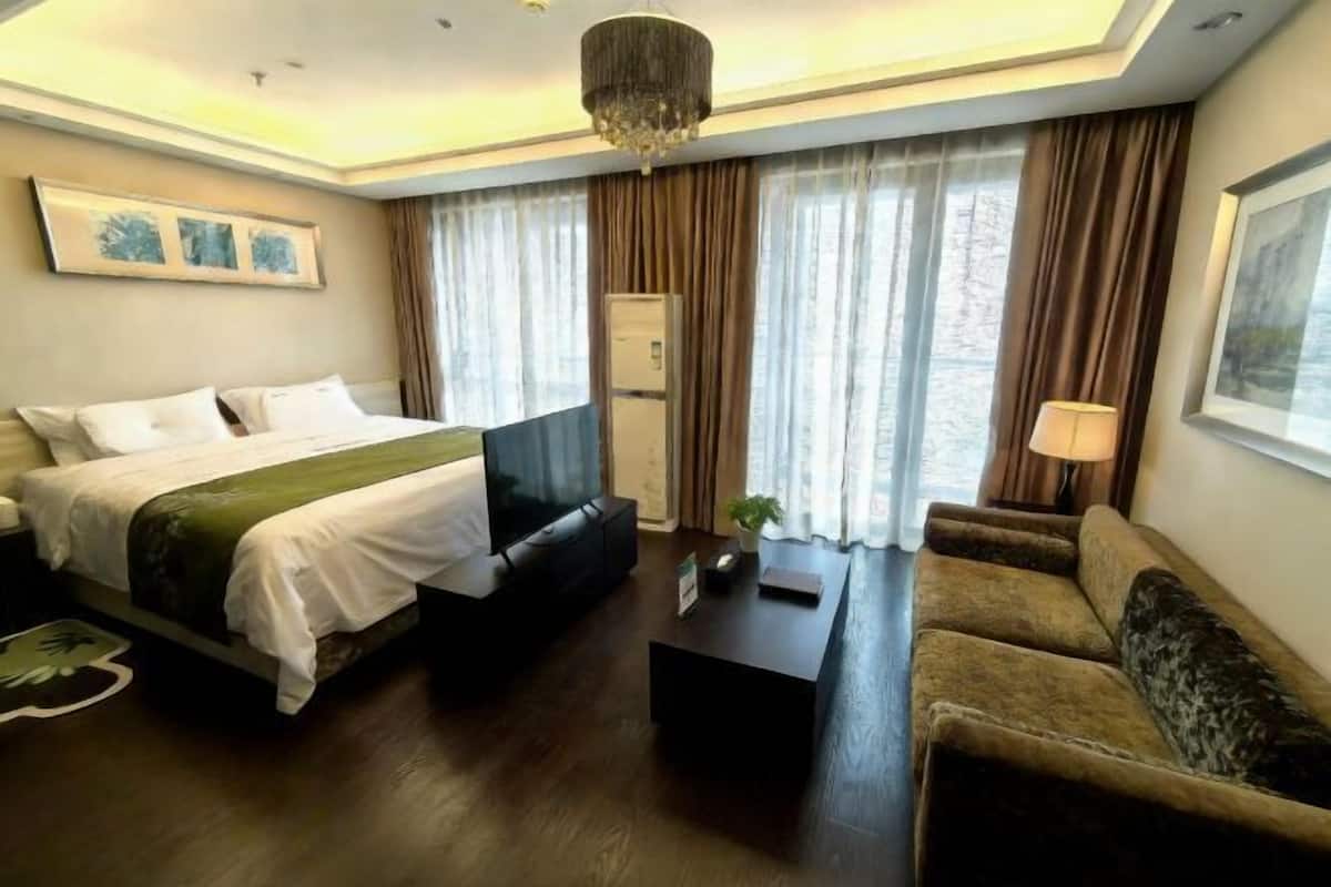 A hotel room with a bed, a sofa, a coffee table, a TV, and a chandelier.