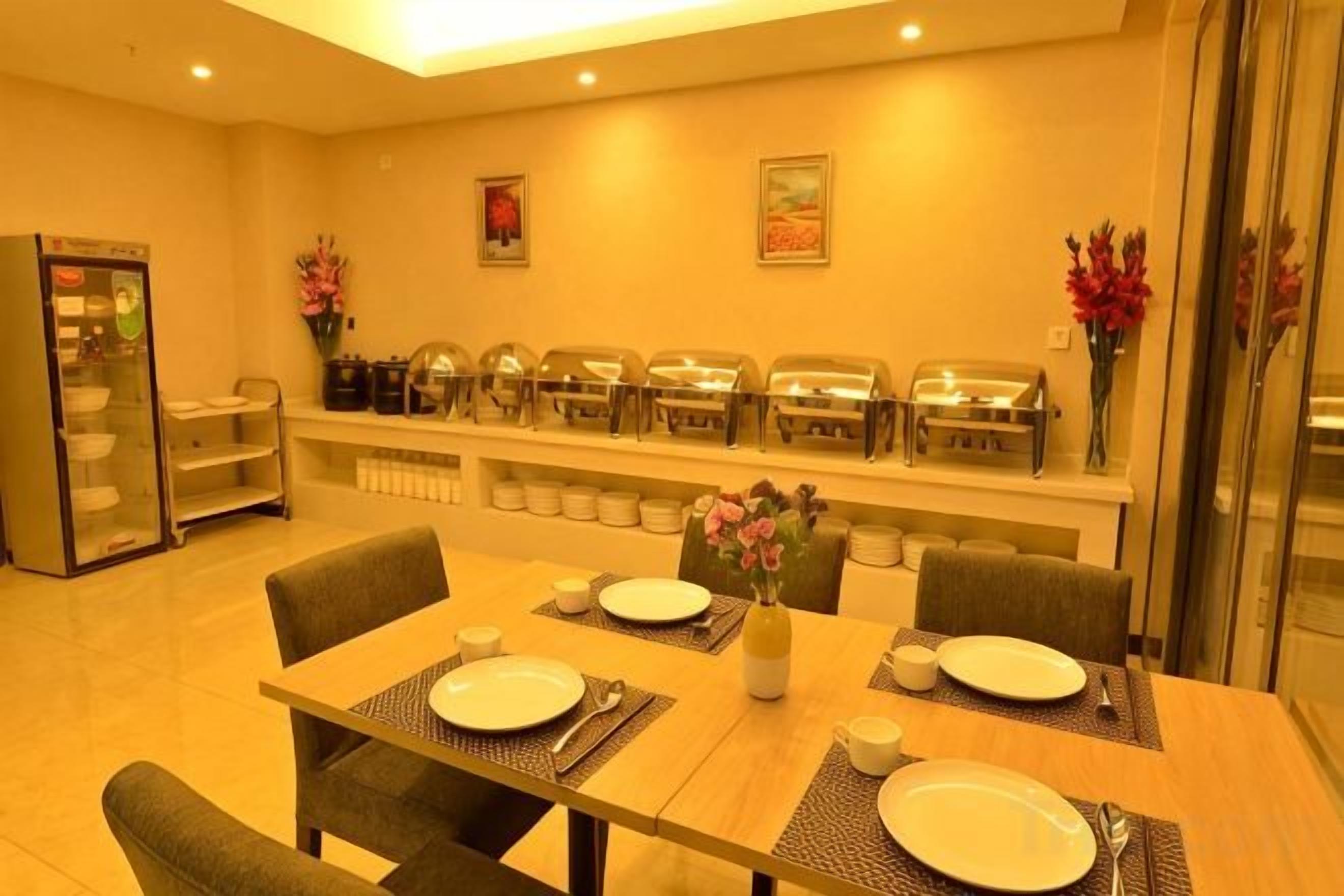 Un comedor con mesas de buffet, un refrigerador y un florero con flores.