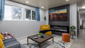 Una sala de estar moderna con chimenea, un sofá, una mesa de centro y un ventanal con cortinas.