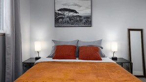 Un dormitorio con cama, dos mesitas de noche, un tocador, un espejo y un cuadro en la pared.