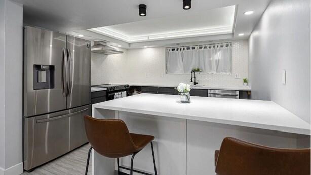 Una cocina moderna con una isla central, electrodomésticos de acero inoxidable y dos taburetes de bar.